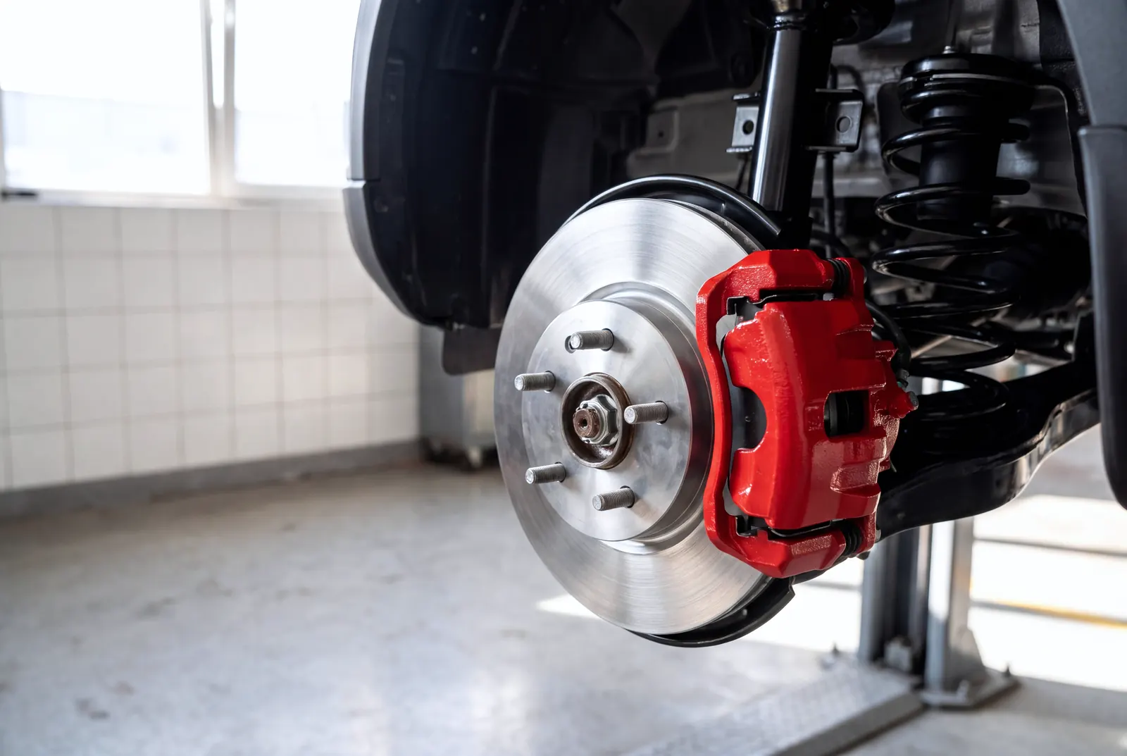 A front brake with the wheel off: a red caliper over a freshly machined rotor, the shop floor out of focus behind.