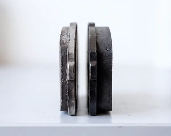 Two brake pads standing on edge, side by side: the worn one on the left has a thin sliver of friction material left, the new one on the right is about four times as thick.