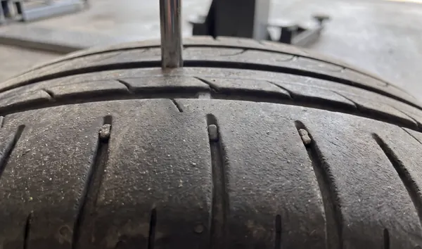 A tread depth gauge pressed into a rear tire groove; the tread is worn nearly level with the wear bars.