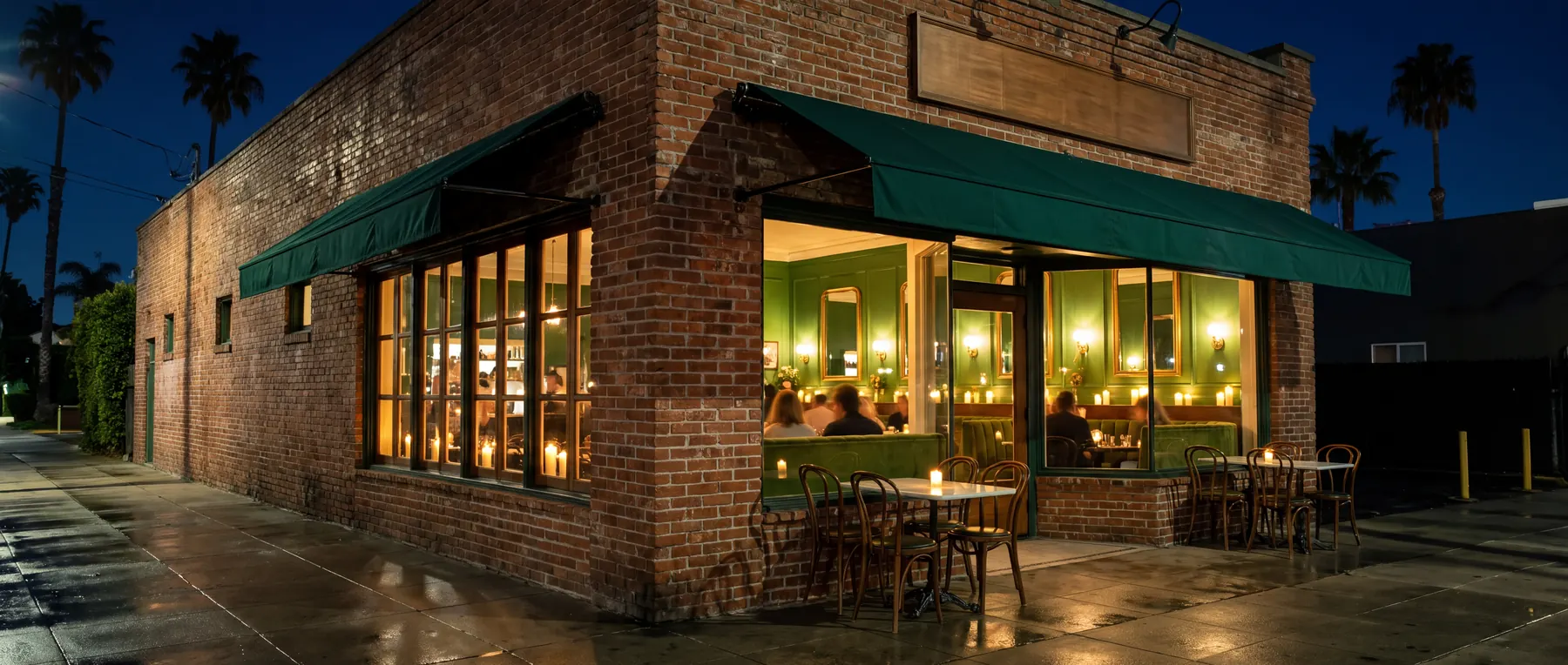 Sauvel's brick corner on York Boulevard at night: green canvas awnings, sidewalk tables with candles, and big windows onto a candlelit green room with banquettes and gilt mirrors, palm trees against a deep blue sky