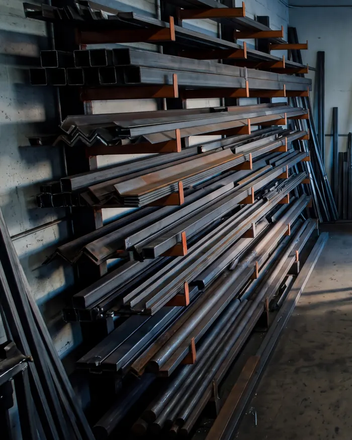 Cantilever racks loaded with square tube, angle and flat bar along the shop wall in cool morning light.