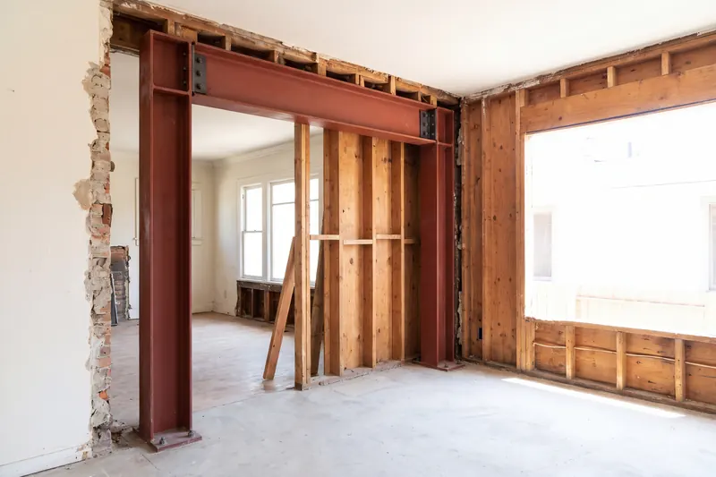 A red oxide primed steel moment frame of two columns and a beam, bolted down inside an opened-up wall during a house remodel.