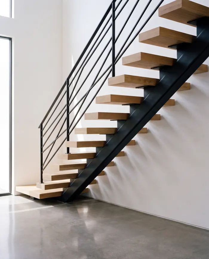 Floating white oak stair treads on a single black steel stringer, with a slim black flat-bar railing, in a bright white room.